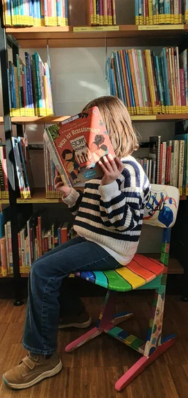 Enfant lisant un livre devant une bibliothèque